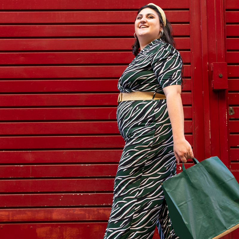 Woman in a stylish plus size outfit, walking confidently with a green bag against a red background.