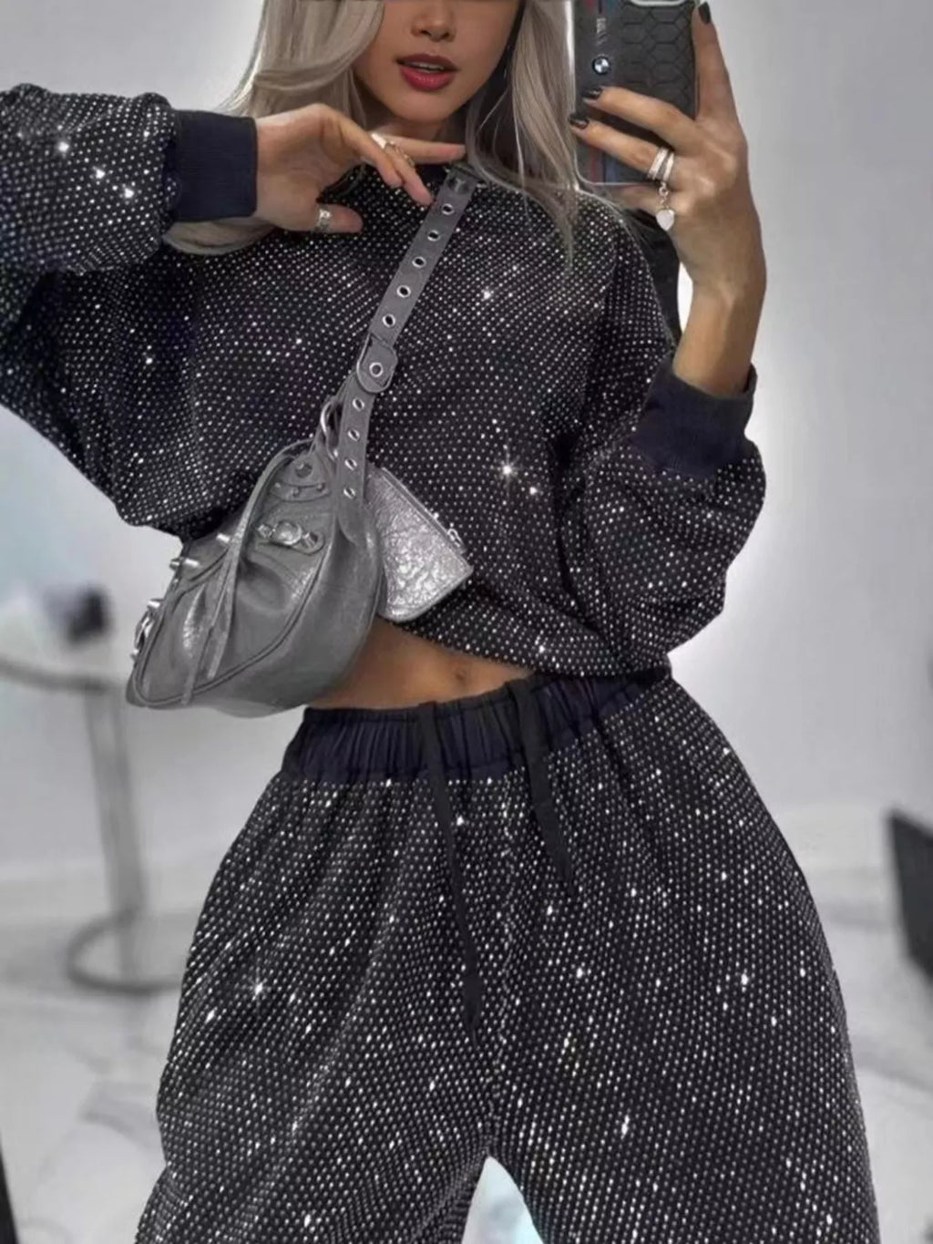 Woman modeling a rhinestone two-piece set featuring a long sleeve top and pants in black with a silver bag.