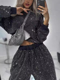 Woman modeling a rhinestone two-piece set featuring a long sleeve top and pants in black with a silver bag.
