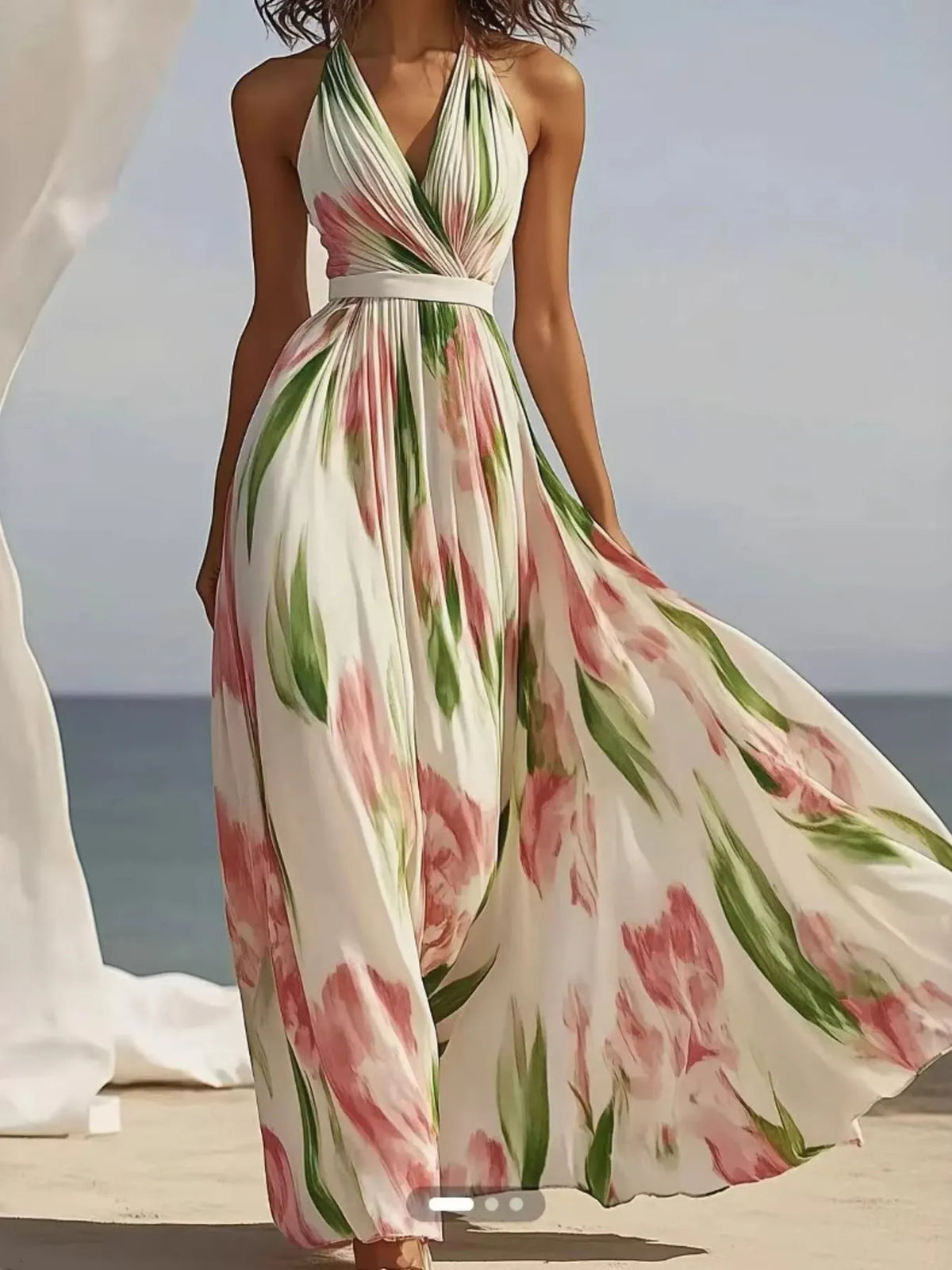 Model wearing a floral print halter neck maxi dress with flowing fabric and vibrant floral patterns against a beach backdrop.