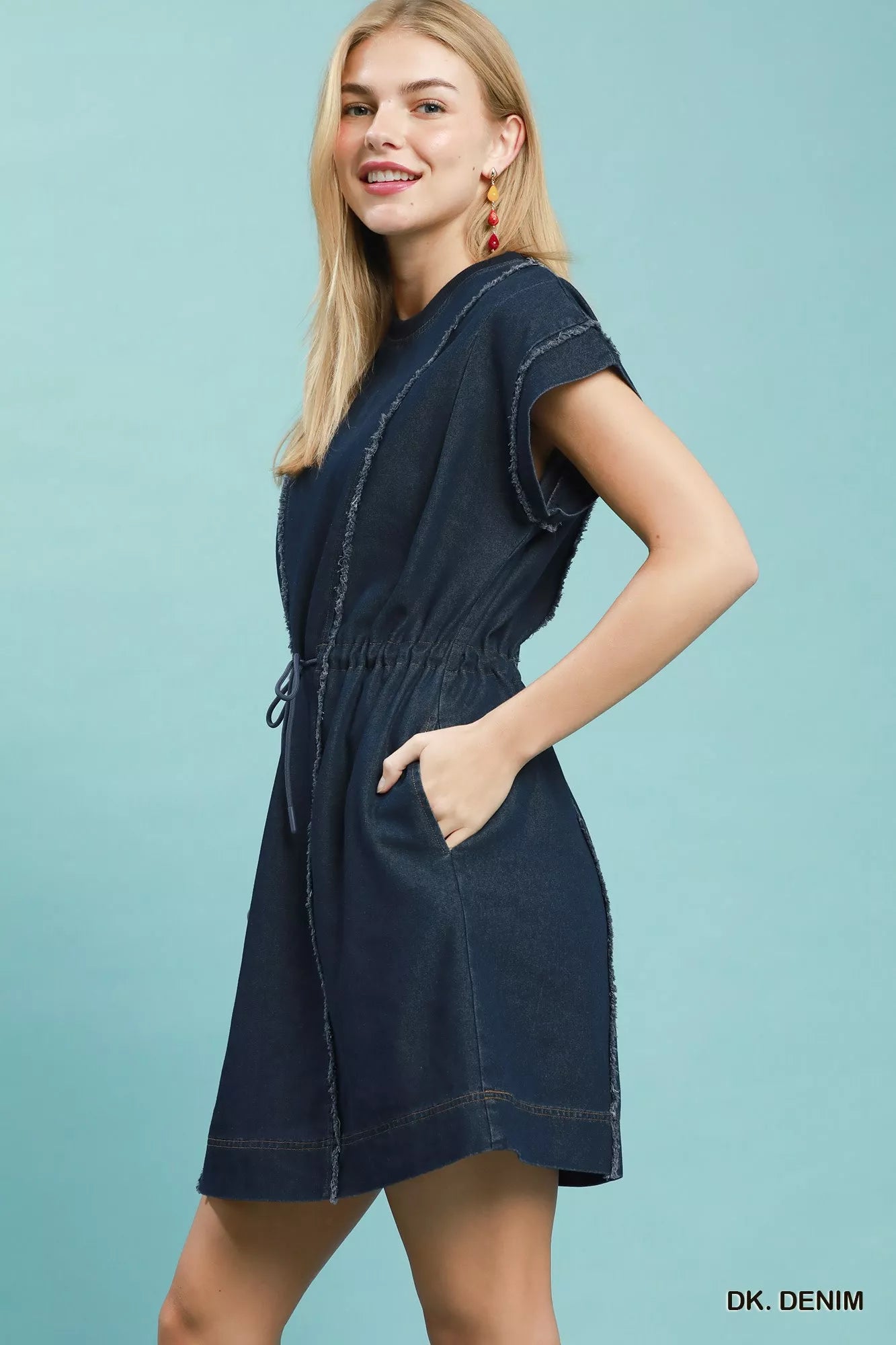 Model showcasing a dark navy denim mini dress with cap sleeves and adjustable drawstring waist.
