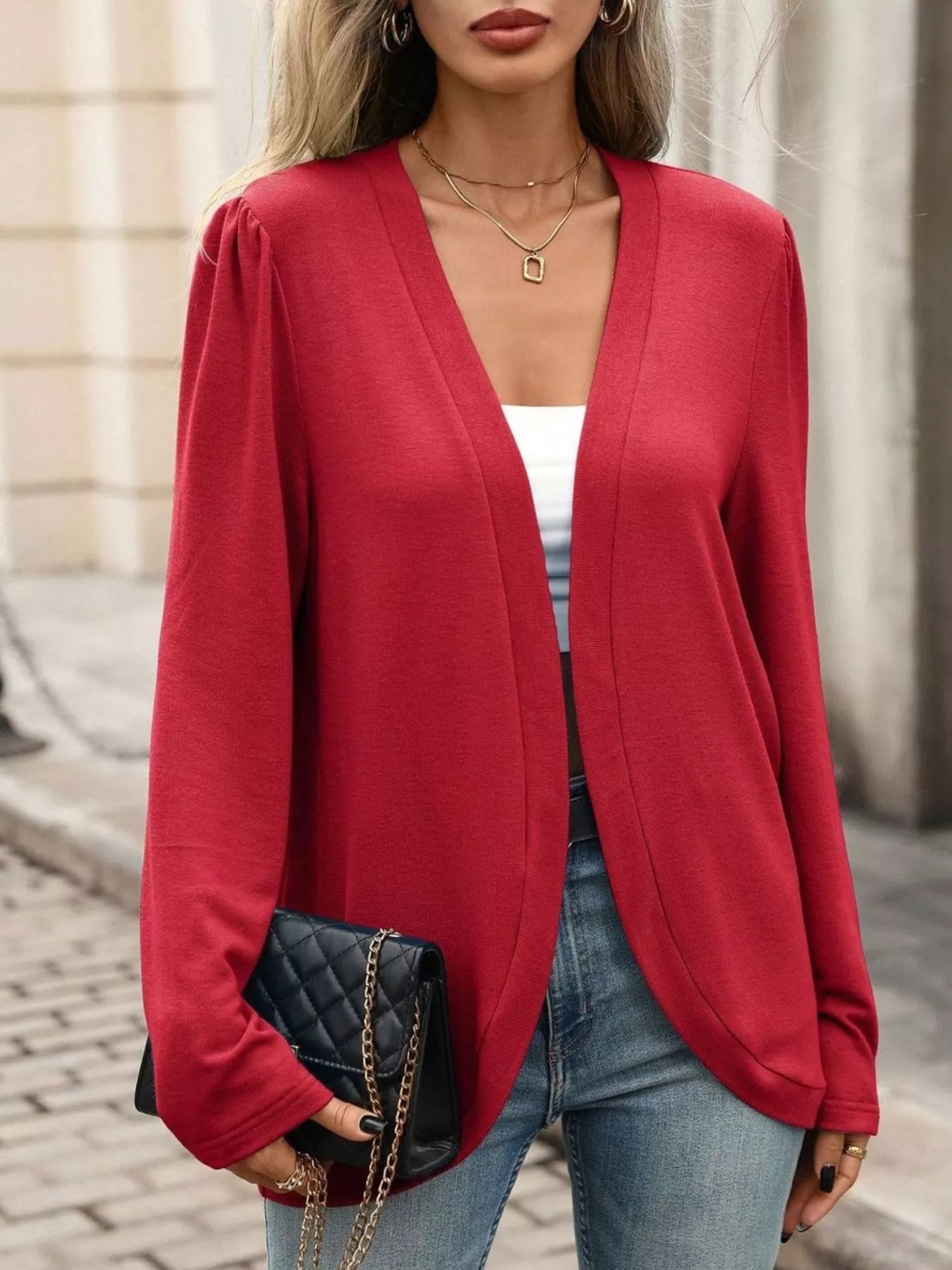 Thin open front cardigan in vibrant red, worn over a white top, paired with stylish jeans and a chic handbag.