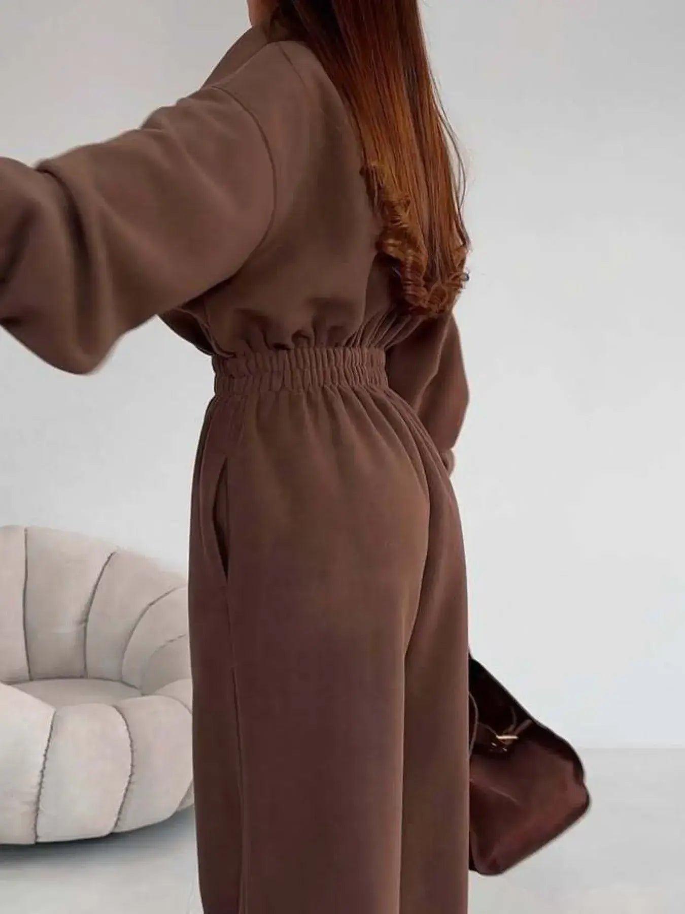 Model showcasing the women's jumpsuit with a zip front and long sleeves in brown, featuring a comfortable elastic waist.