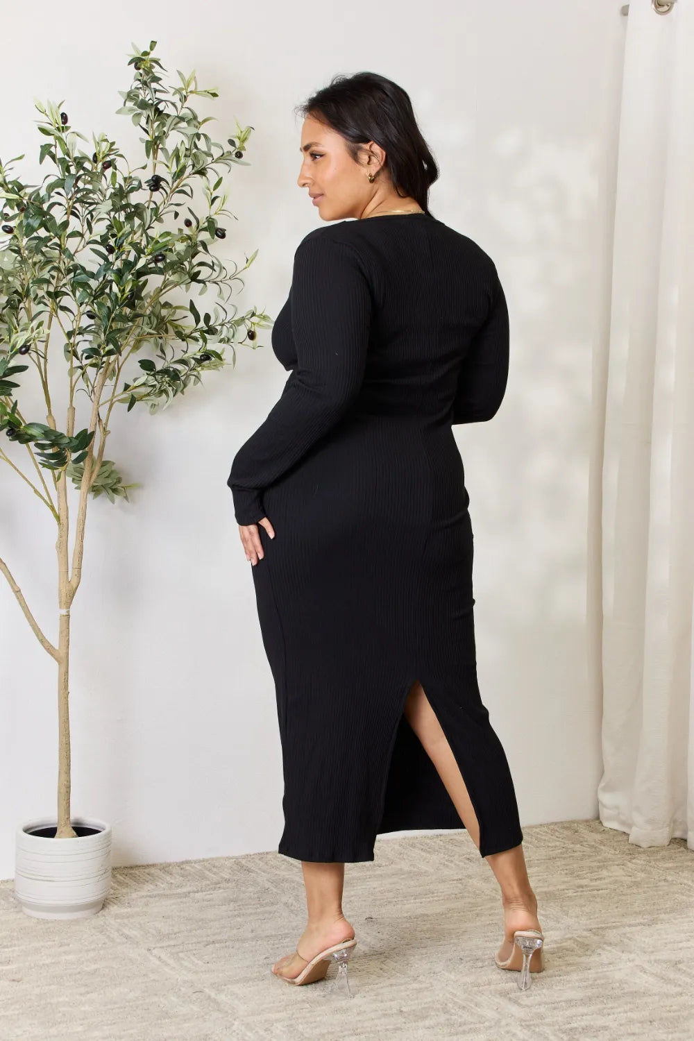 A model showcases a fashionable midi dress with a slit detail, featuring ribbed fabric and long sleeves.