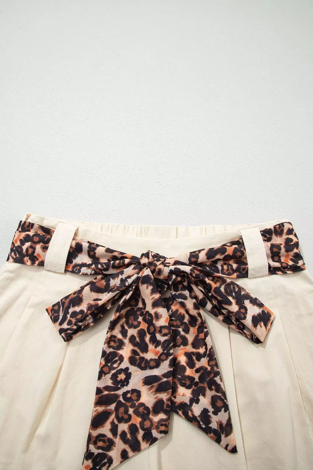 Close-up of tailored pleated shorts with a leopard print belted waist detail.
