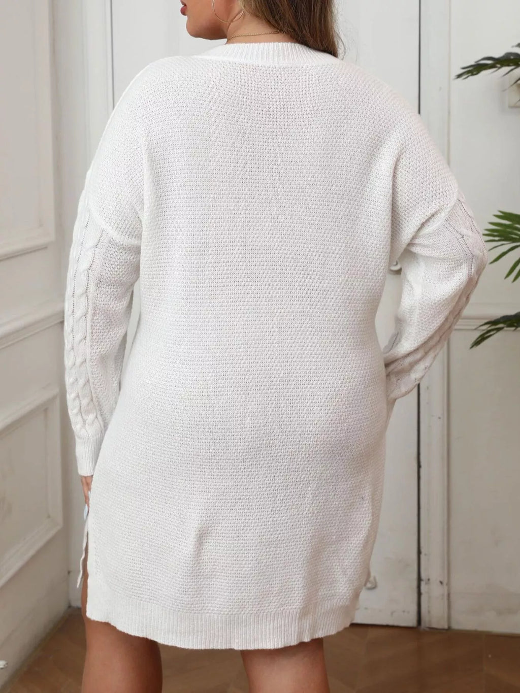 Back view of a model wearing a plus size sweater dress in white, featuring cable knit design and relaxed fit.