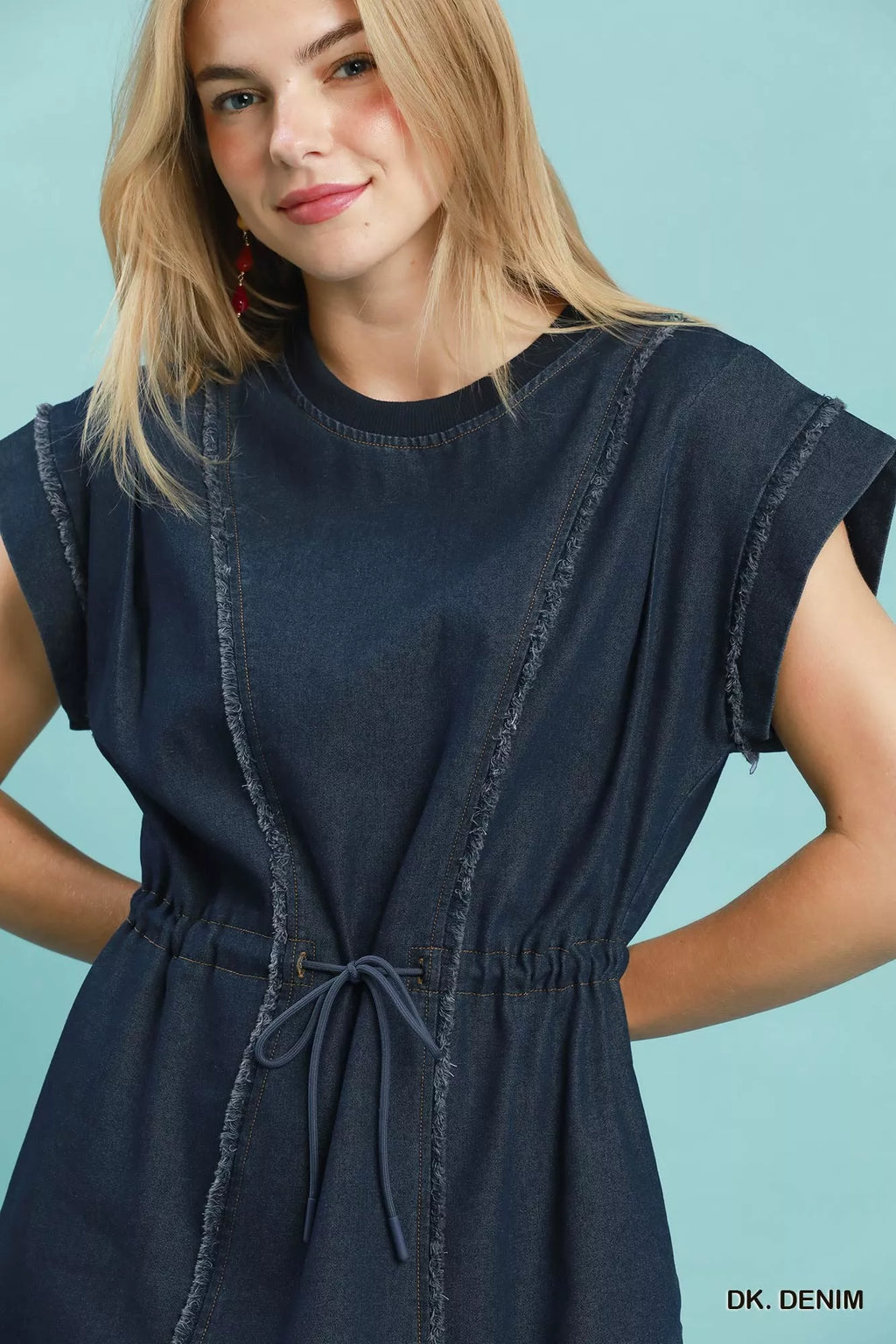 Model wearing a dark navy denim mini dress with cap sleeves and drawstring waist for a relaxed fit.