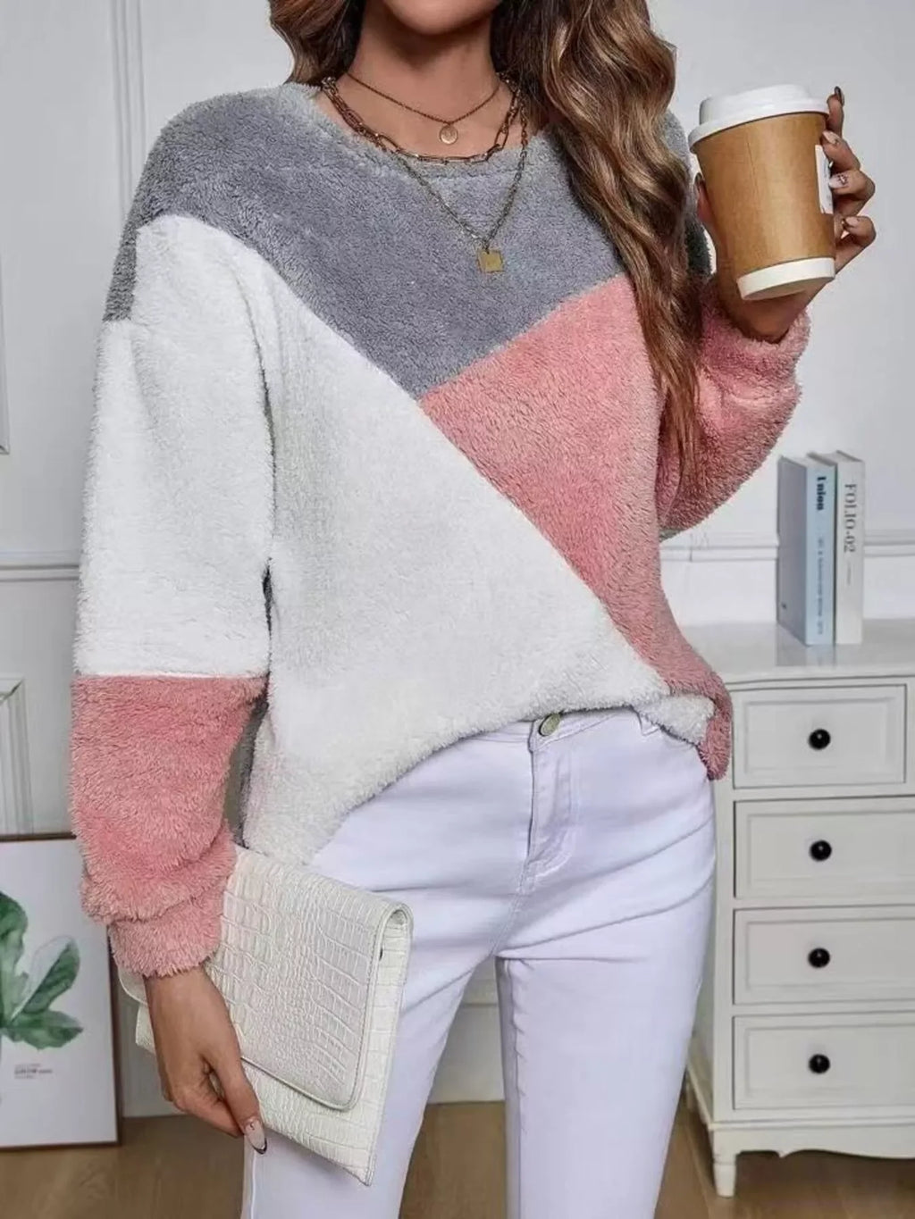 Stylish woman in pink grey fuzzy knit sweatshirt holding coffee, featuring playful color block design.