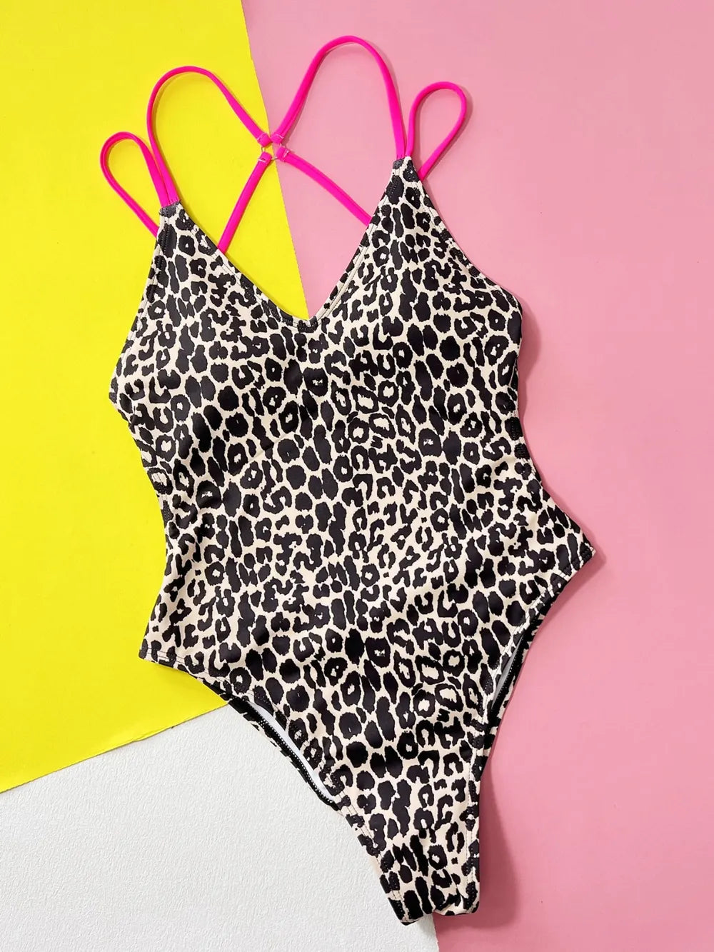 Fashionable swimwear in a leopard print plunge thong one-piece with pink spaghetti straps on a colorful background.