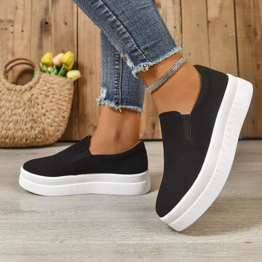 Black slip-on platform shoes showcased on a woman with distressed jeans, ideal for casual and stylish outfits.