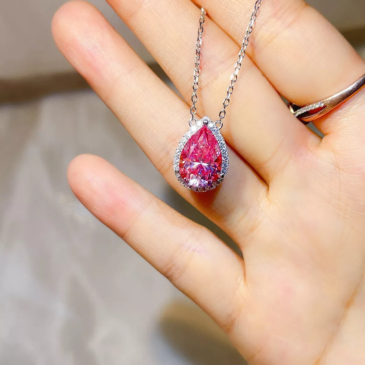 925 sterling silver pendant necklace featuring a stunning pink Moissanite stone held in a hand.