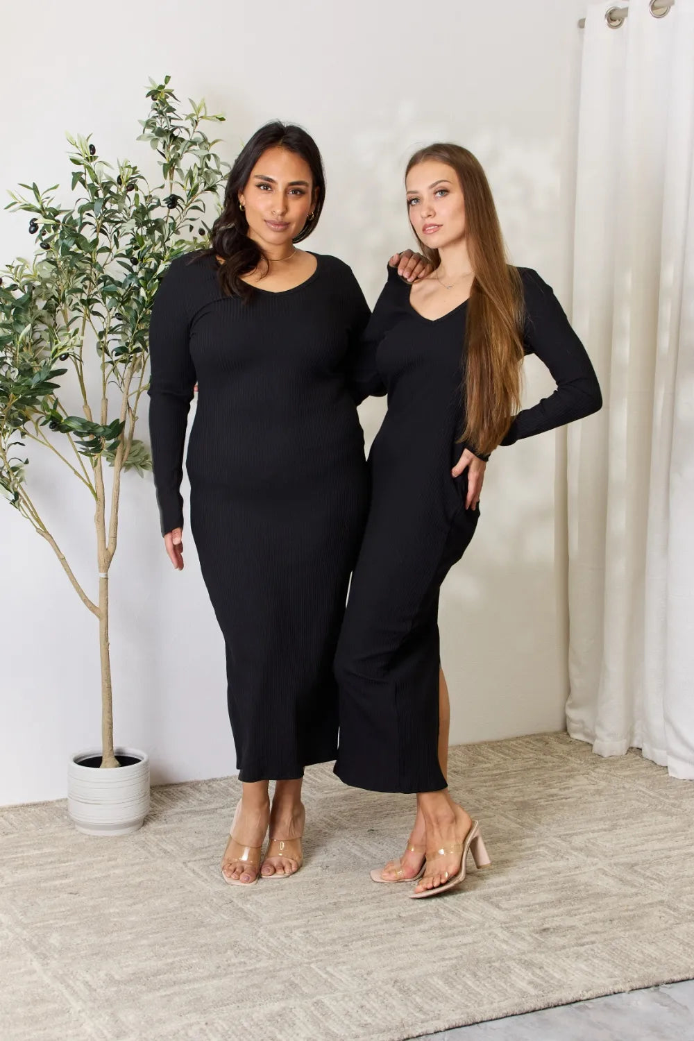 Two models showcasing a fashionable midi dress with long sleeves and side slit detail in black.