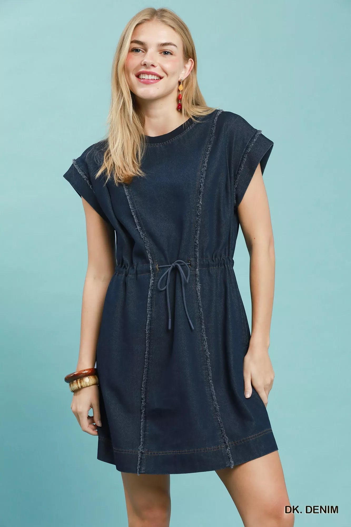 Model wearing a dark navy denim mini dress with cap sleeves and drawstring waist, featuring raw frayed seams.