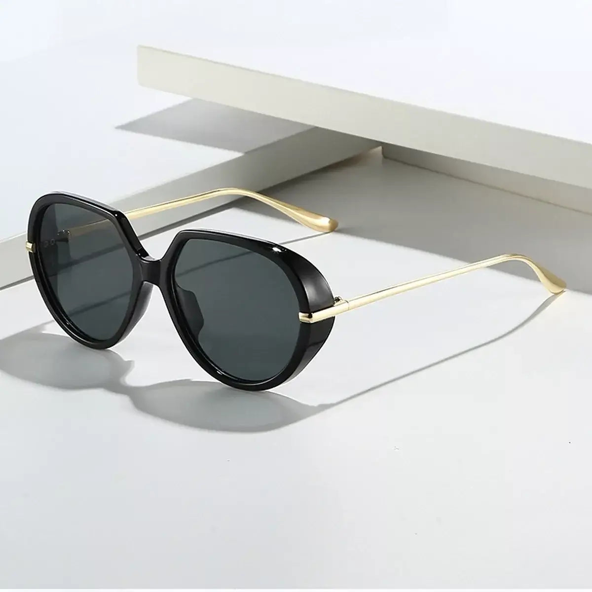 Stylish oversized tinted sunglasses with black frames and gold accents placed on a minimalist surface.