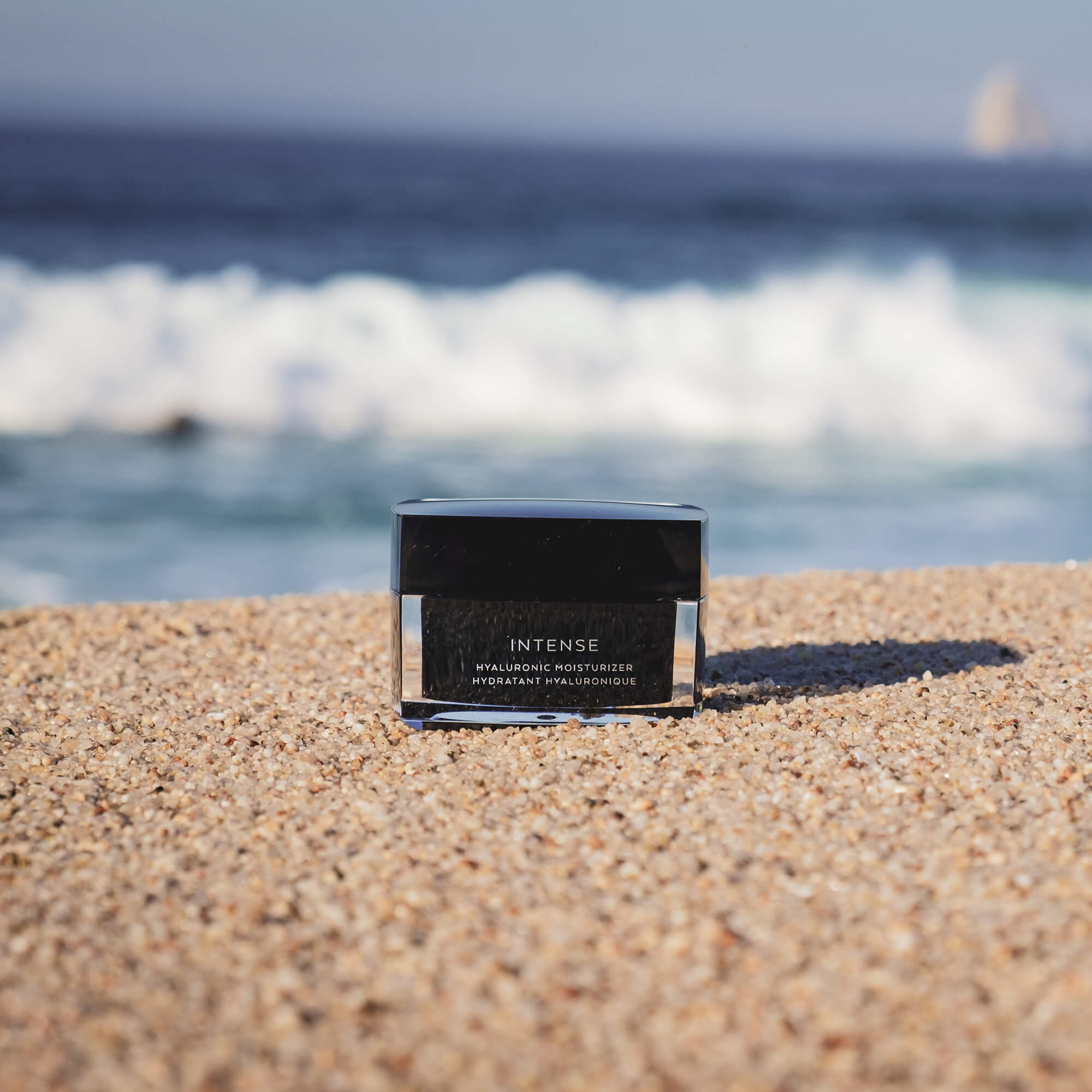 Hyaluronic moisturizer for dry skin placed on a sandy beach with waves in the background.