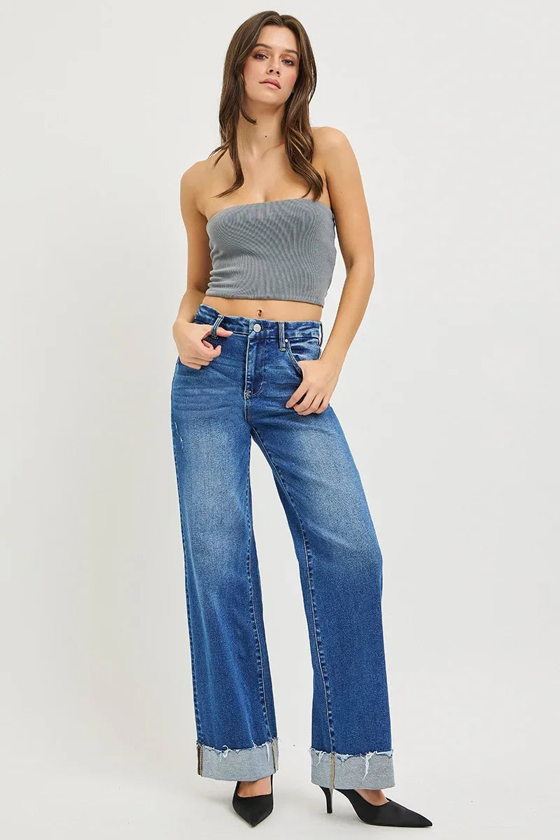 Woman wearing a gray bandeau crop top and wide-leg cuffed blue jeans with black heels