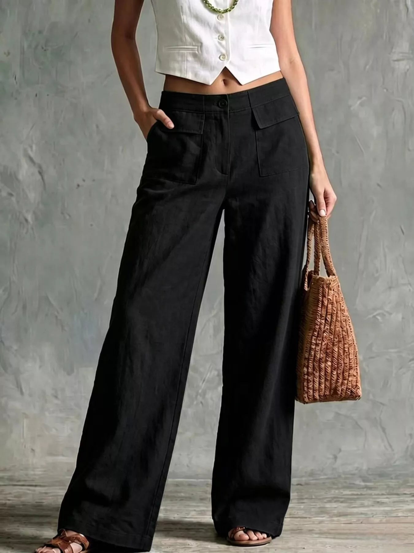 Model wearing stylish plus size wide leg pants in black, paired with a white cropped top and a woven bag.