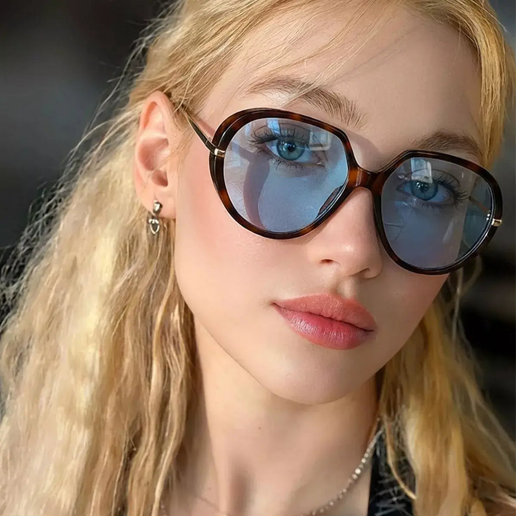 Oversized tinted sunglasses worn by a model with blonde hair and blue tinted lenses.
