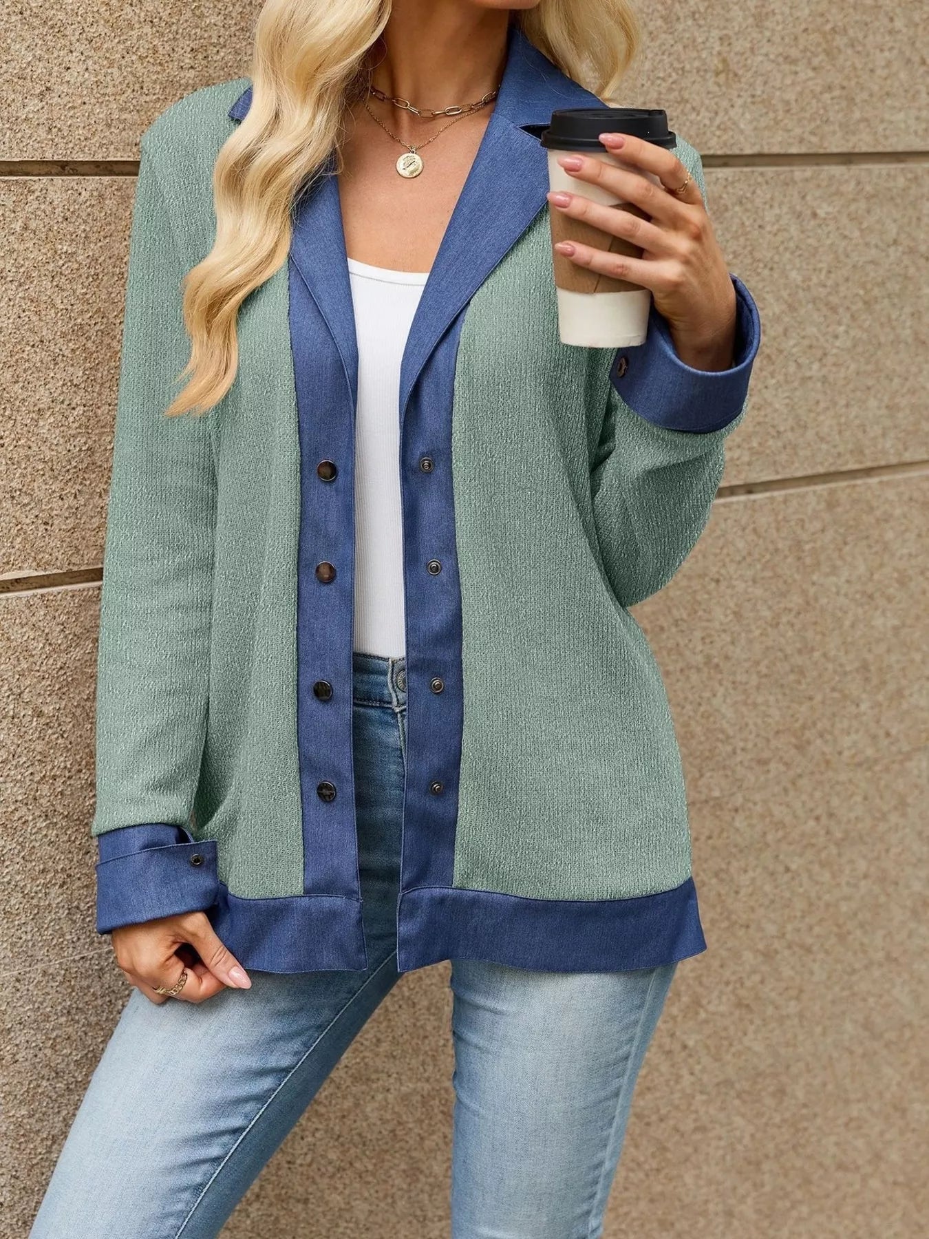 Model wearing a contrast denim lapel jacket in green with blue accents, holding a coffee cup against a textured wall.