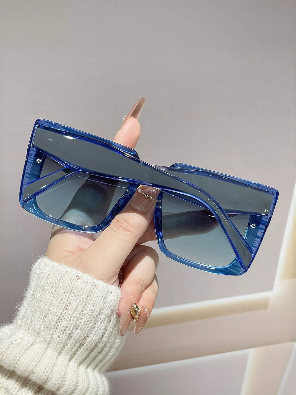Oversized square sunglasses UV400 in blue held by hand, featuring a modern and lightweight design.