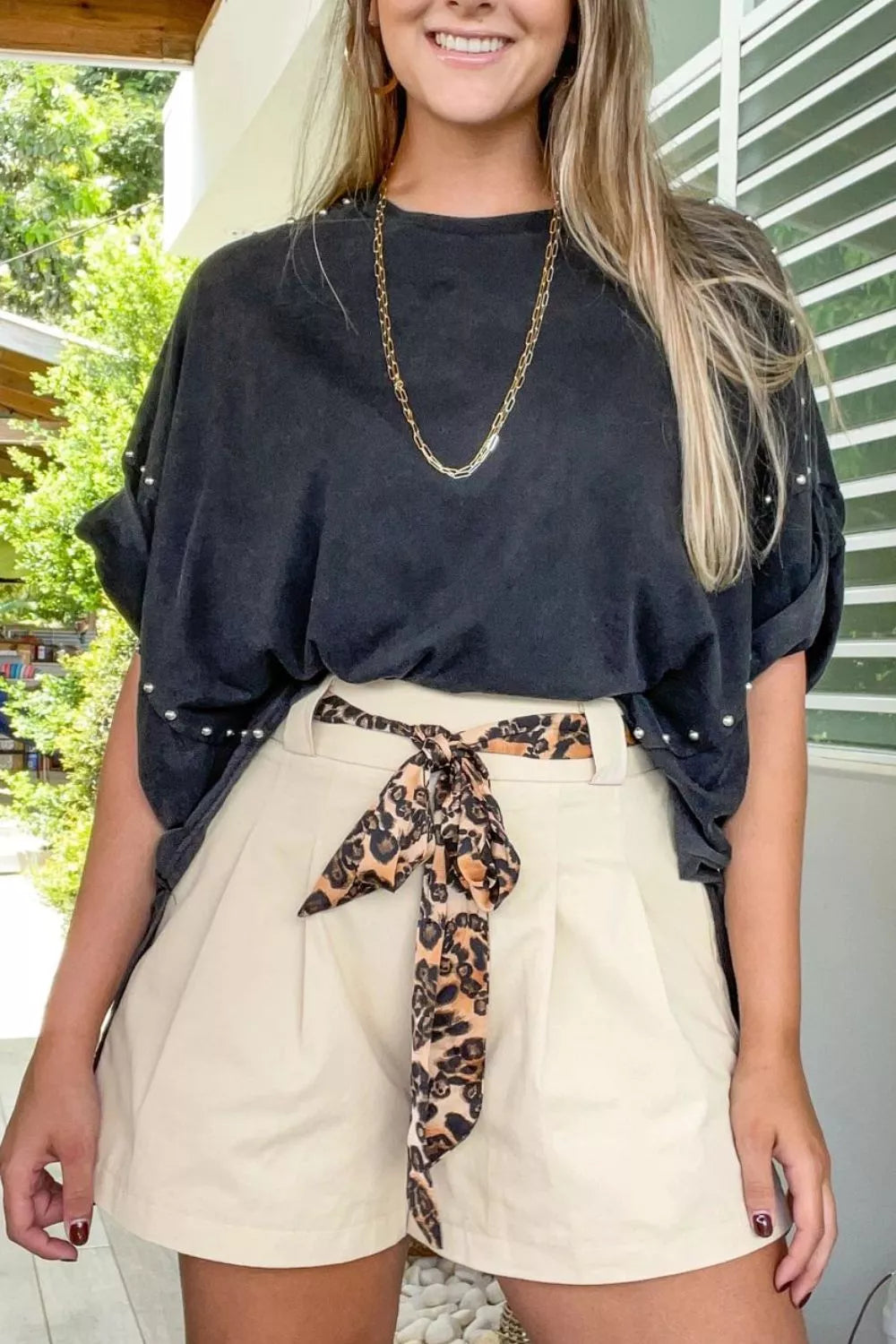 Woman wearing tailored pleated shorts with a belted waist and a loose black top, showcasing a stylish casual look.