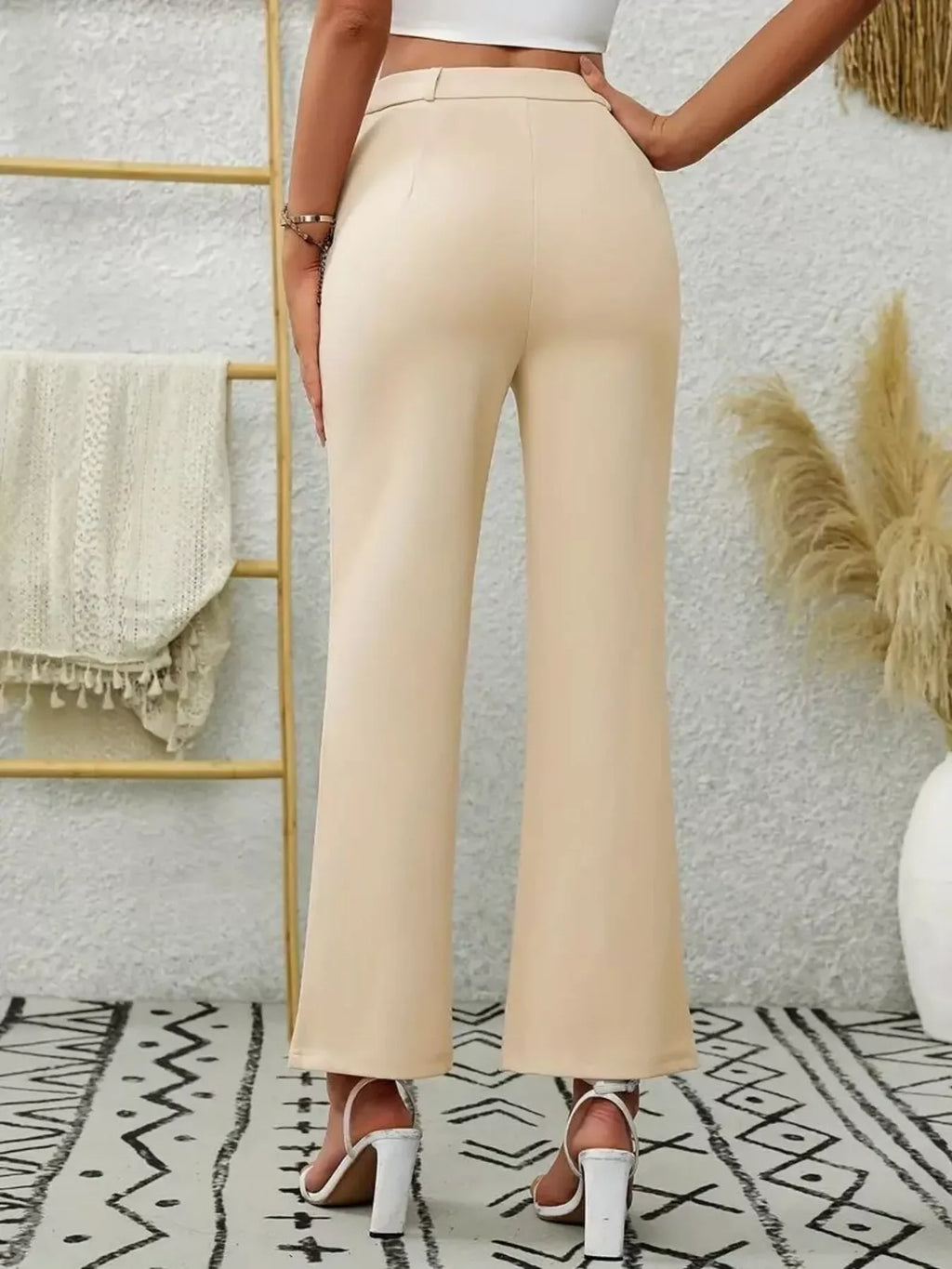 Woman's back view wearing light beige high waist flare pants against a textured wall and abstract patterned floor.