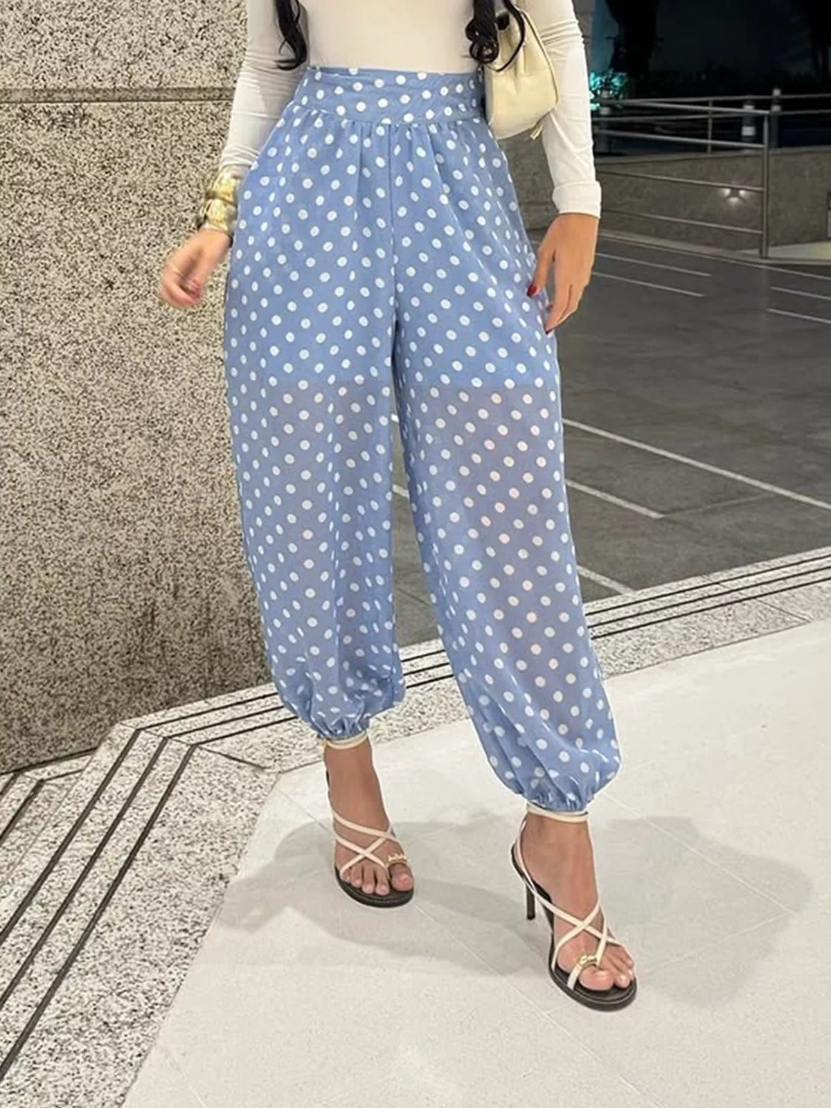 Woman wearing polka dot wide leg pants, styled with a fitted top and heels, on a city walkway.