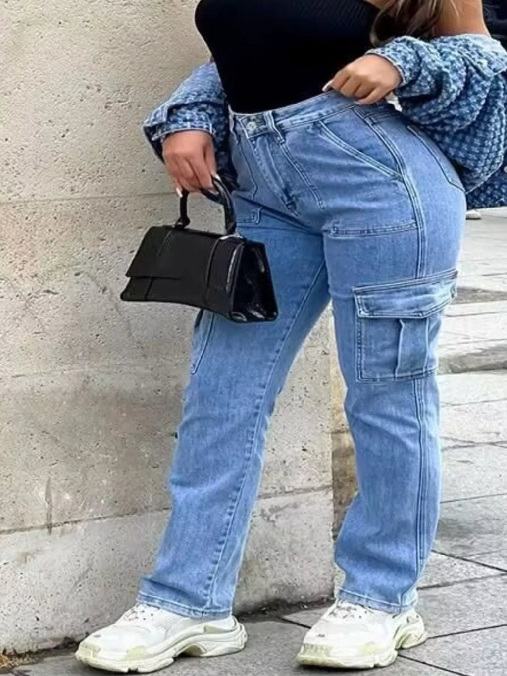 Light wash cargo jeans with pockets styled with a black top and handbag, showcasing a casual and trendy look.