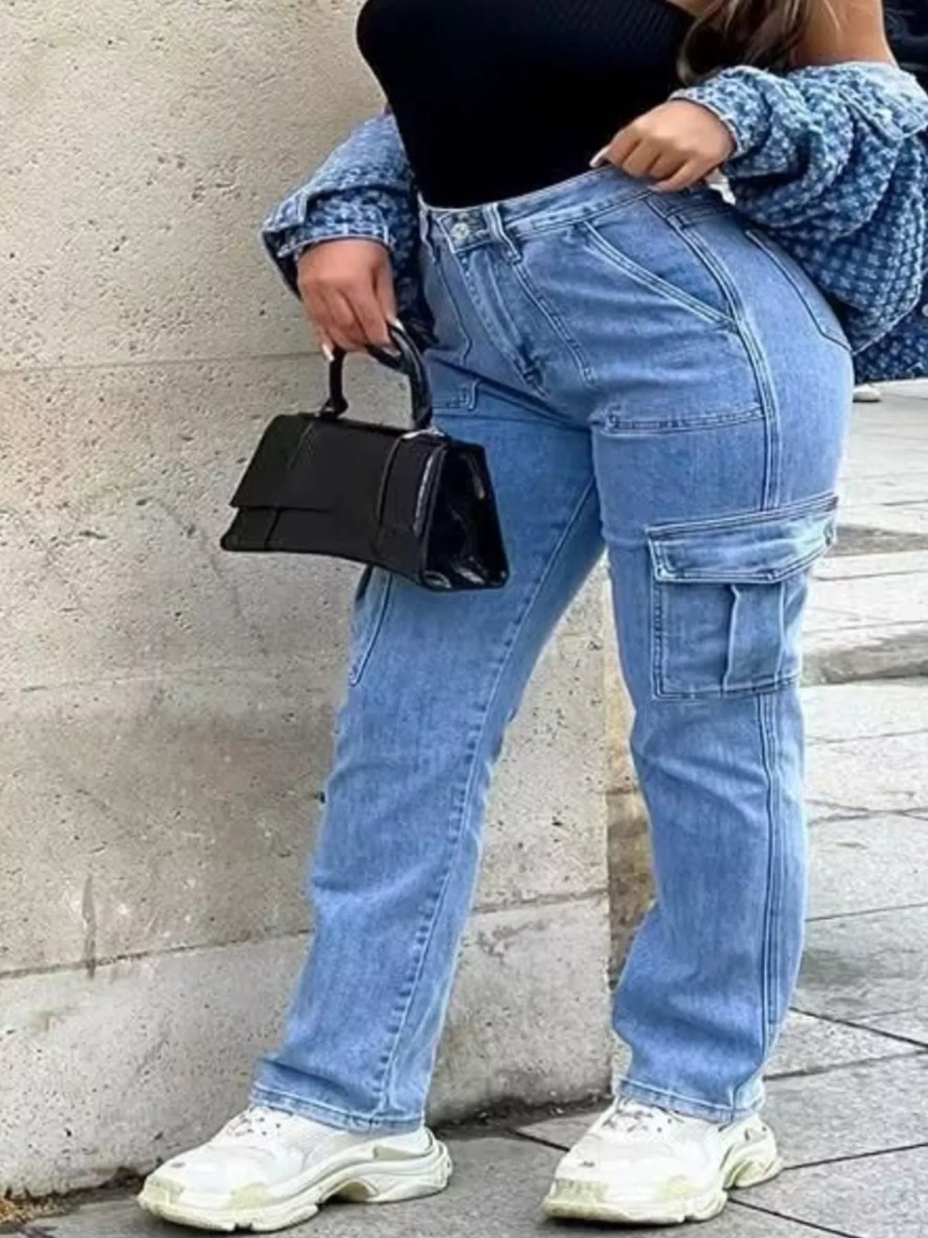 Light wash cargo jeans with pockets styled with a black top and handbag, showcasing a casual and trendy look.