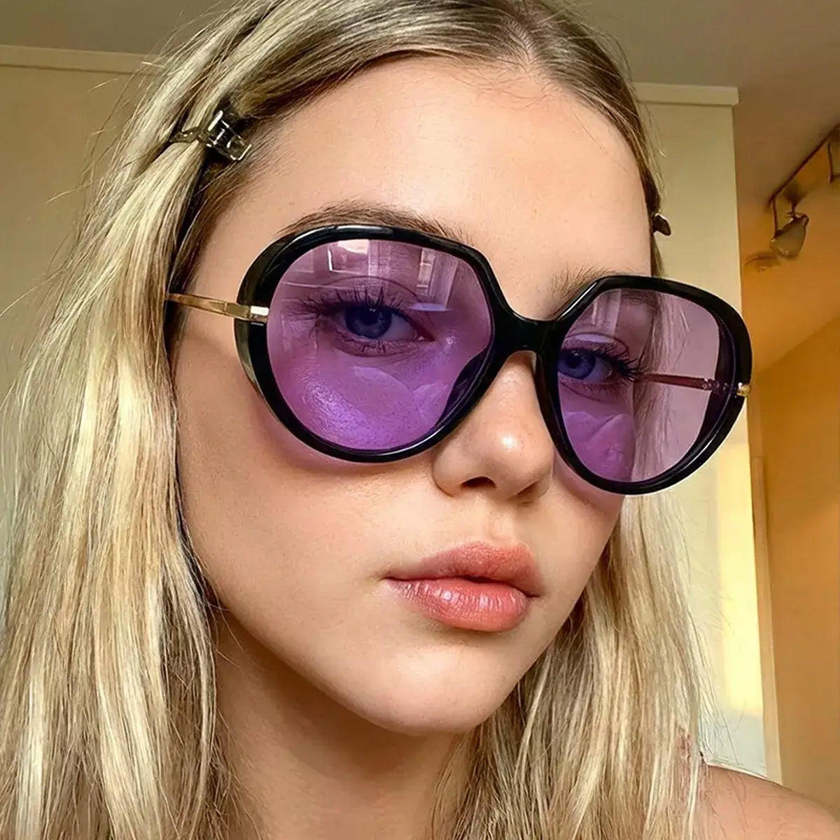 Close-up of a model wearing oversized tinted sunglasses with purple lenses, showcasing a stylish and bold look.