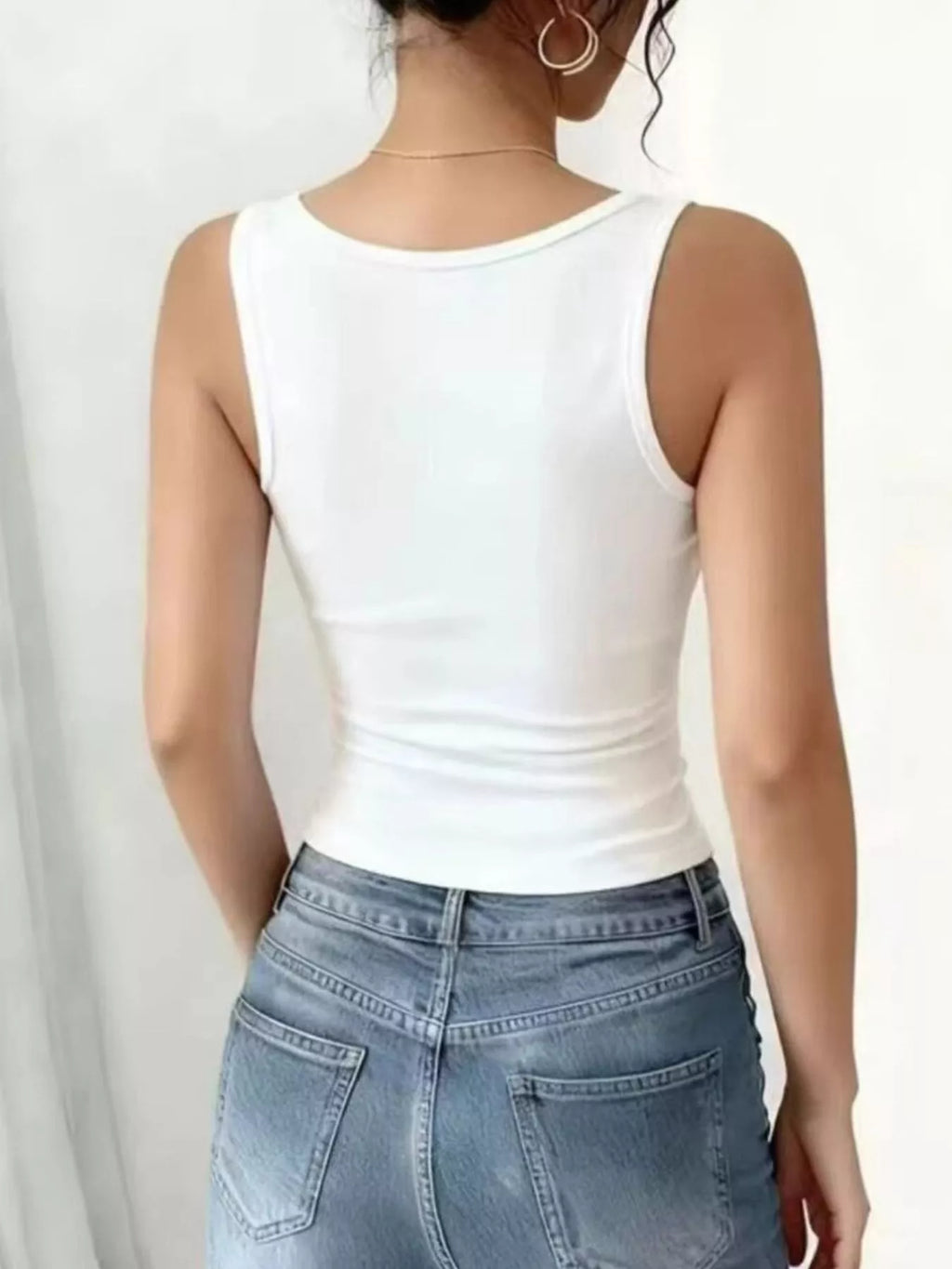 Back view of a model wearing a white lace trim tank top paired with denim shorts.
