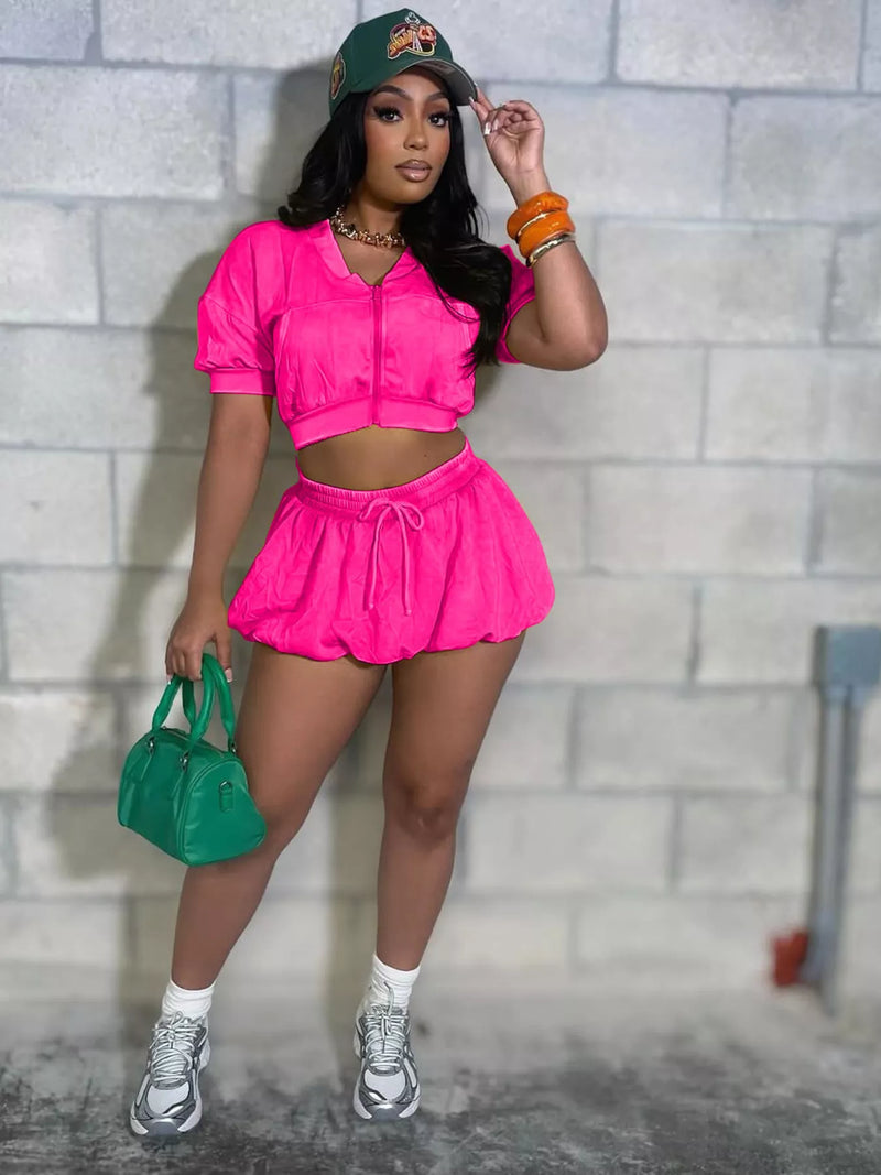 Woman in a pink women's crop top and shorts set with a zip-up top and drawstring shorts, paired with accessories.