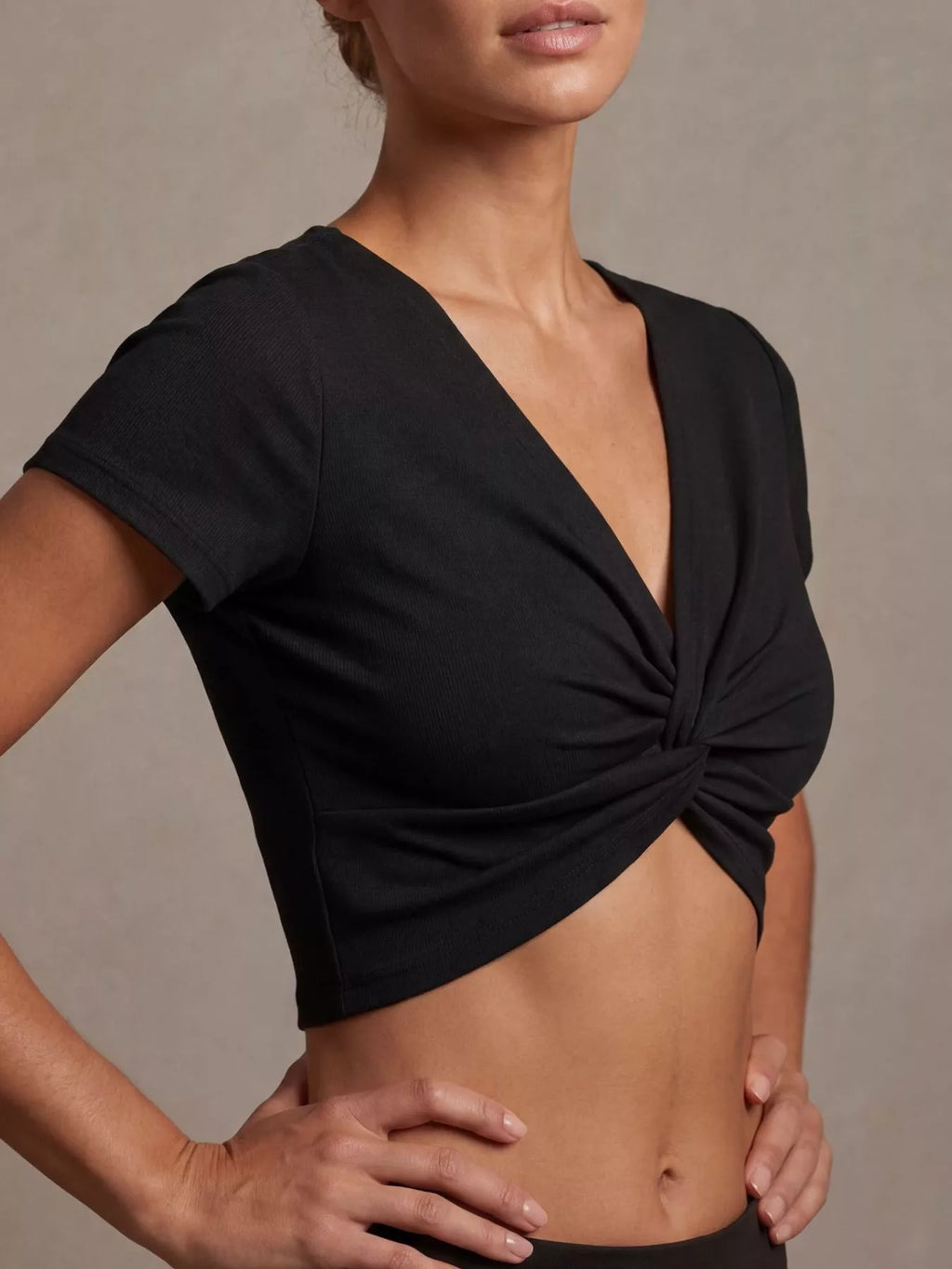 Model wearing a twist front shirt cropped top in black with short sleeves and twisted front design.
