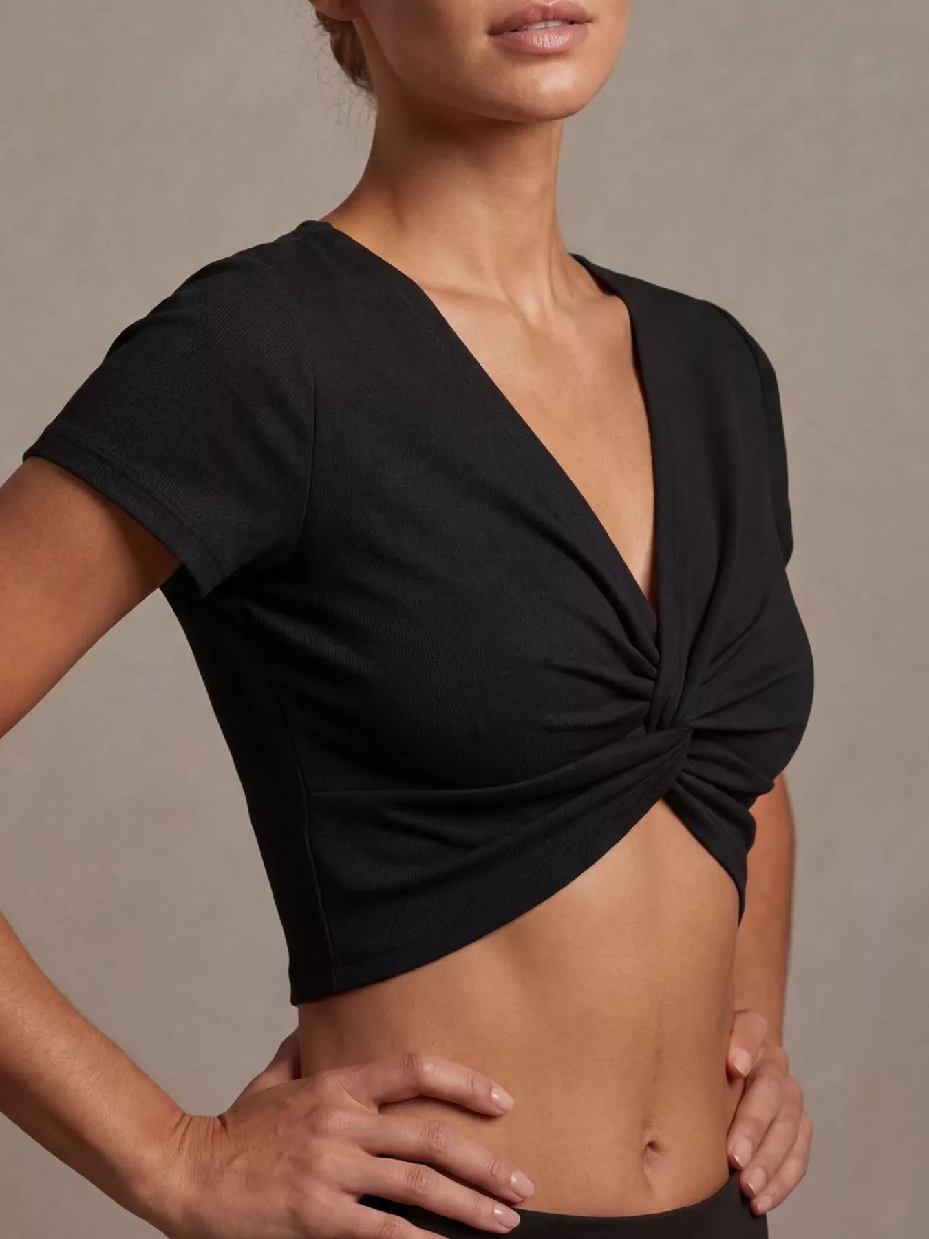 Model wearing a twist front shirt cropped top in black with short sleeves and twisted front design.