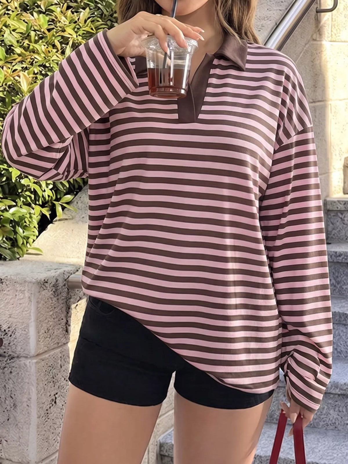 A woman wearing a vintage striped polo shirt long sleeve top, holding a drink, showcasing a relaxed style.