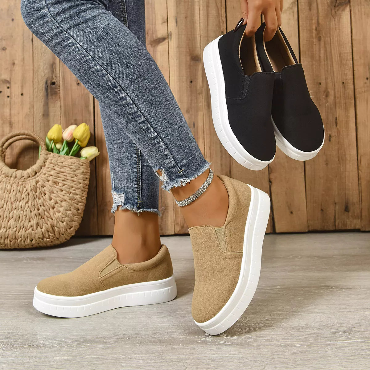 Woman wearing slip-on platform shoes in beige and black against a wooden background.