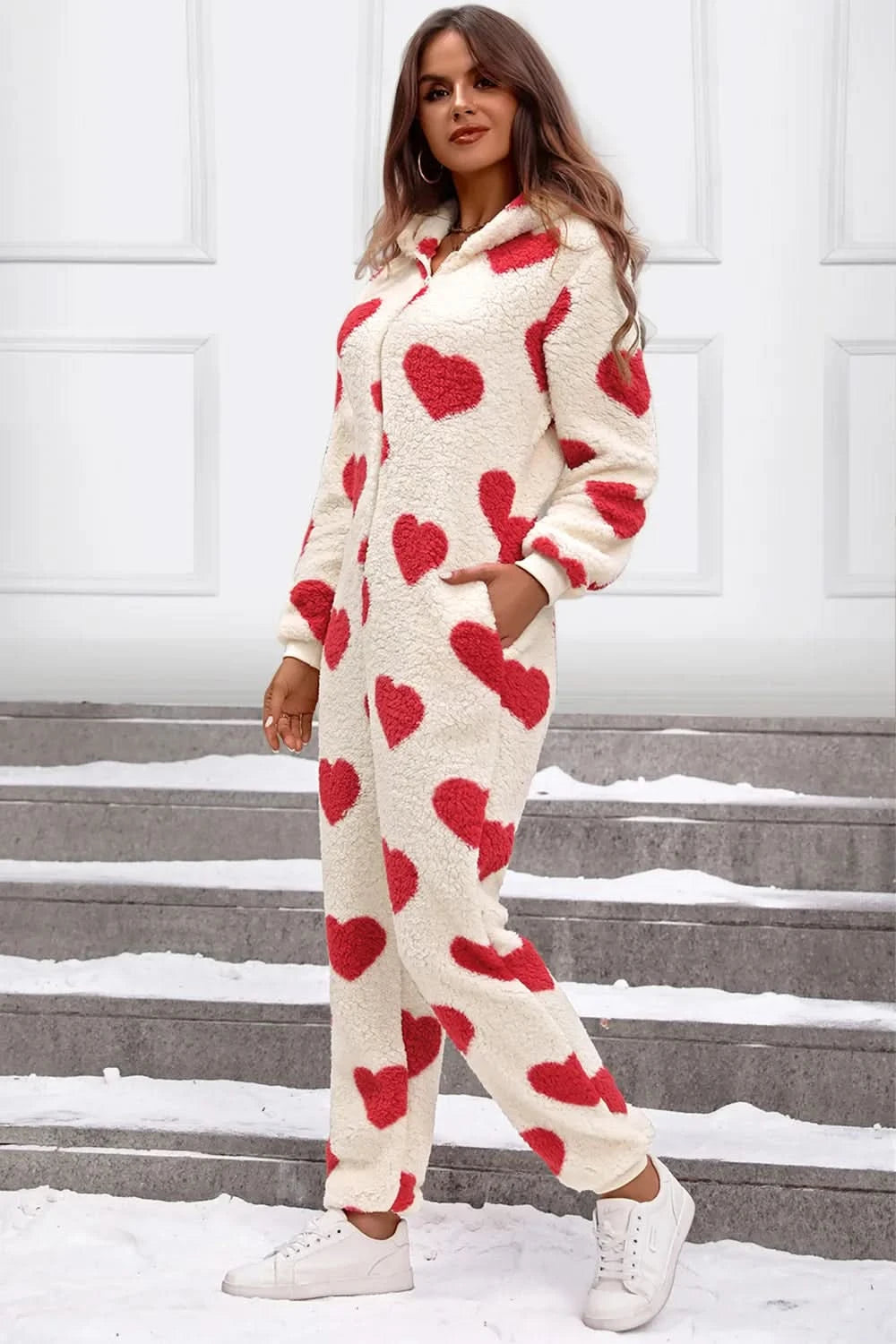 Woman wearing a fuzzy heart lounge jumpsuit standing on steps in the snow, showcasing cozy and cute style.