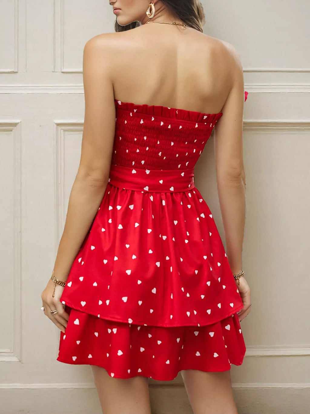 Back view of a woman wearing a smocked mini dress with a layered skirt and heart patterns in red.