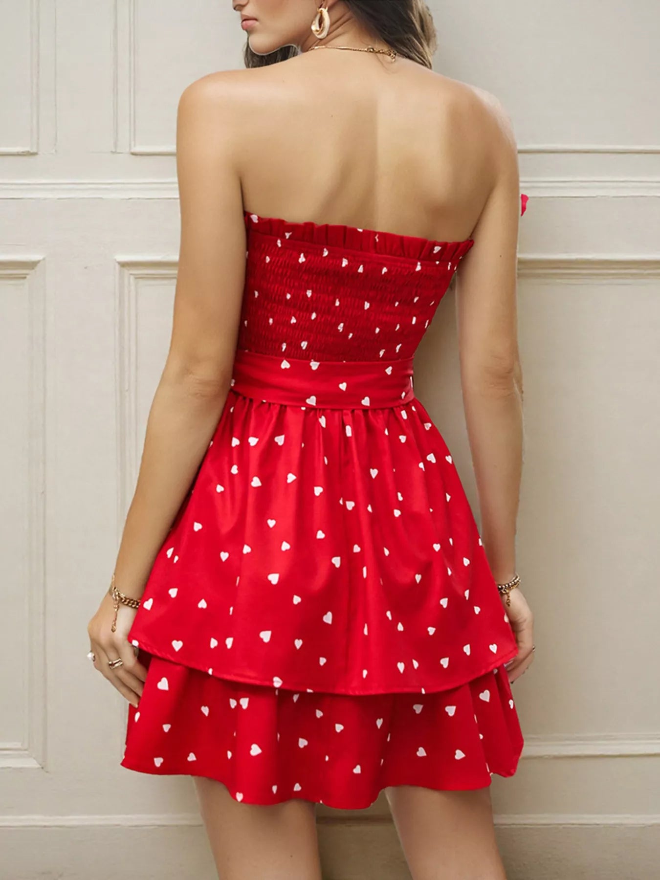 Back view of a woman wearing a smocked mini dress with a layered skirt and heart patterns in red.