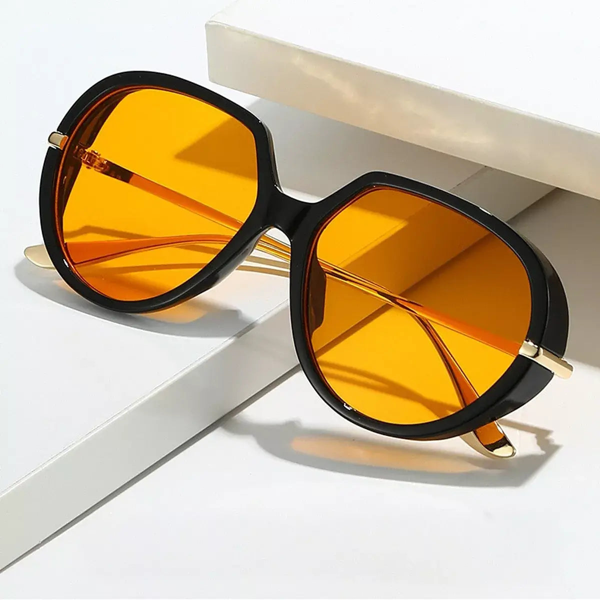 Oversized tinted sunglasses with orange lenses and black frames resting on a white surface.