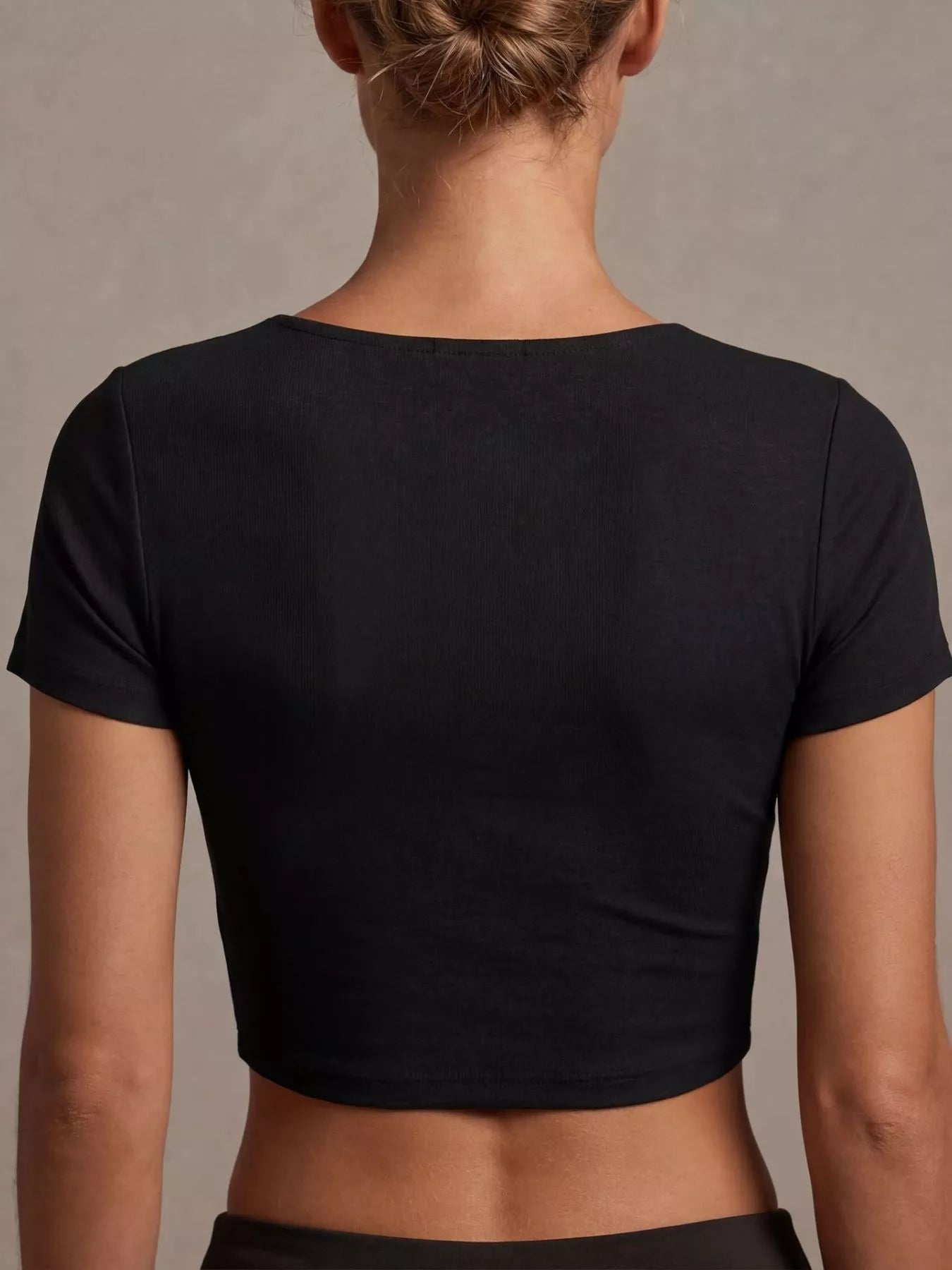 Back view of a twist front shirt cropped top in black, showcasing a fitted design and short sleeves.